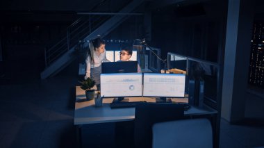 Güvenilir İşadamı Masaüstü Bilgisayarını Kullanıyor, Onun Kadın Proje Yöneticisi Özel Görevleri, Hesaplama ve Stratejik Hareketleri Açıklıyor. Büyük Şirket Ofisinde Profesyonel İnsanlar Geceleyin Geç Saatlere Kadar Çalışıyor