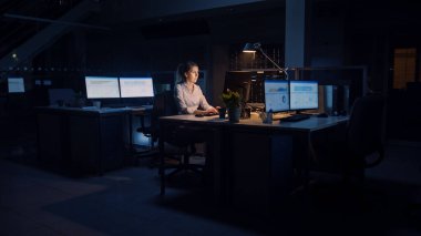 Ofiste Gece Geç Saatlere Kadar Çalışmak: İş kadını Masaüstü Bilgisayarı Kullanıyor, Analiz Ediyor, Belgeleri Kullanıyor, Sorunları Çözüyor, Önemli Projeyi Bitiyor. Çalışkan Hırslı Genç İşçi