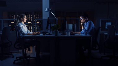 Ofiste Gece Geç Saatlere Kadar Çalışmak: İşçiler Masaüstü Bilgisayarlarını Kullanıyor, Analiz Ediyor, Belgeleri Kullanıyor, Sorunları Çözüyor, Önemli Projeyi Bitiriyorlar. Çalışkan, hırslı, genç iş adamları. Yan Görünüm