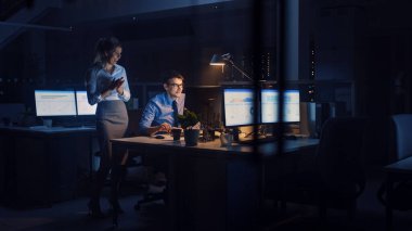 İşadamı Masaüstü Bilgisayarı Kullanıyor, Onun Kadın Proje Yöneticisi Özel Görevleri, Hesaplama ve Stratejik Hareketleri Açıklıyor. Büyük Şirket Ofisinde Profesyonel İnsanlar Geceleyin Geç Saatlere Kadar Çalışıyor