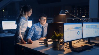 İşadamı Masaüstü Bilgisayarı Kullanıyor, Onun Kadın Proje Yöneticisi Özel Görevleri, Hesaplama ve Stratejik Hareketleri Açıklıyor. Büyük Şirket Ofisinde Profesyonel İnsanlar Geceleyin Geç Saatlere Kadar Çalışıyor