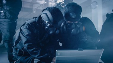 Maskeli Özel Tim Tüfekli Polis Memurları Masa ve Bilgisayarlı Karanlık Ofis Binası 'nda. Asker Taktiksel Saldırı Planlamak için Dizüstü bilgisayar açtı.