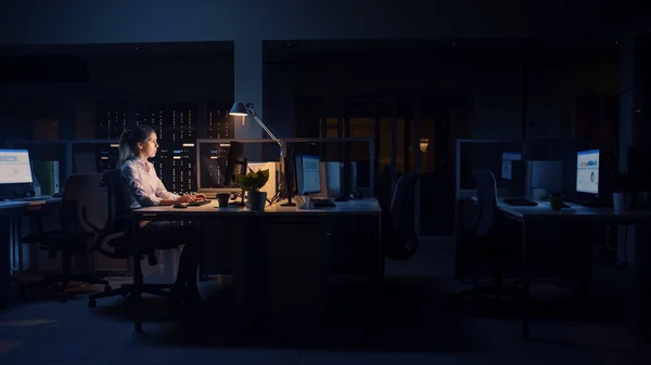 Praca do późna w nocy w biurze: Bizneswoman używa komputera stacjonarnego, Analizowanie, Korzystanie z dokumentów, Rozwiązywanie problemów, Zakończenie ważnego projektu. Staranny, ambitny, młody pracownik. Widok z boku — Zdjęcie stockowe