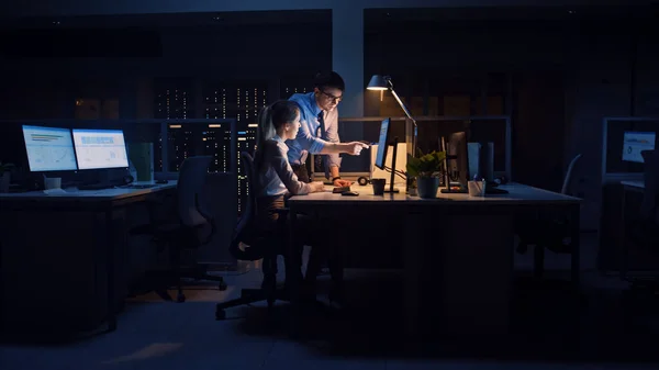 Selbstbewusster Geschäftsmann verwendet Desktop-Computer, seine weibliche Projektmanagerin erklärt spezifische Aufgaben, Kontoführung und strategische Schritte. Berufstätige spät in der Nacht in Großunternehmen — Stockfoto