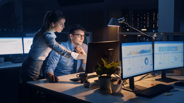 Affärsman använder stationär dator, hans kvinnliga projektledare förklarar specifika uppgifter, kontohantering och strategiska rörelser. Professionella människor sent på natten i Big Corporate Office — Stockfoto