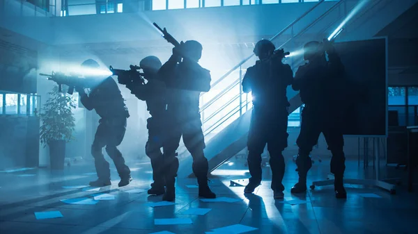 Masked Fireteam of Armed SWAT Police Officers Storm a Dark Seized Office Building with Desks and Computers Солдати з гвинтівками і ліхтарями переходять уперед і прикривають оточення. — стокове фото
