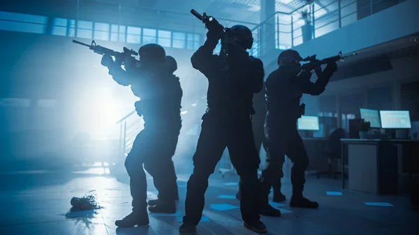 Escouade masquée d'officiers de police armés du SWAT dans un hall d'un immeuble de bureaux sombre avec bureaux et ordinateurs. Soldats avec fusils et lampes de poche Survoile et housse Environs. — Photo