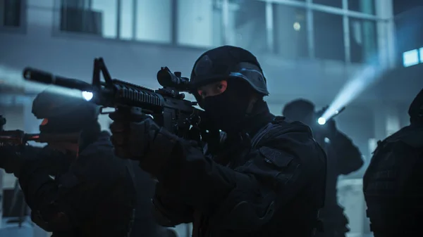Maskované komando ozbrojených policistů SWAT stojí v temně obsazené kancelářské budově se stoly a počítači. Vojáci s puškami a baterkami Průzkum a obal. — Stock fotografie
