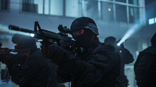 Masked Squad of Armed SWAT Police Officers Stand in Dark Seized Office Building with Desks and Computers. Soldiers with Rifles and Flashlights Surveil and Cover Surroundings.