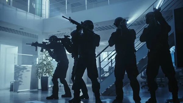 Masked Squad of Armed SWAT Police Officers Stand in Dark Seized Office Building with Desks and Computers. 지렛대와 섬광등을 가지고 있는 군인들의 수면 덮개와 수면 위를 덮고 있다. — 스톡 사진