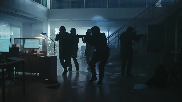 Equipo Enmascarado de Oficiales de Policía Armados SWAT se mueven en un Salón de un edificio de oficinas oscuro con escritorios y computadoras. Soldados con rifles y linternas Vigilancia y cobertura de los alrededores. — Foto de Stock