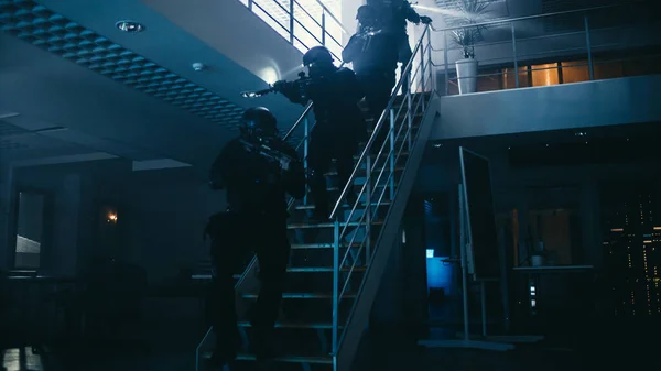 Masked Squad of Armed SWAT Police Officers Run Down the Stairs from a Second Floor in a Dark Office Building. Soldiers with Rifles and Flashlights Move Forwards and Cover Surroundings. — Stock Photo, Image