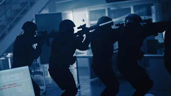 Fegyveres SWAT rendőrökből álló álarcos csapat vonuljon sorba egy sötét lefoglalt irodaépület előcsarnokában, íróasztalokkal és számítógépekkel. Katonák puskákkal és zseblámpákkal Surveil and Cover Környék. — Stock Fotó