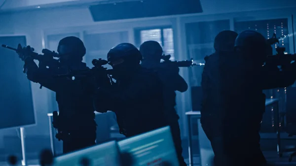 Masked Squad of Armed SWAT Police Officers Stand in Dark Seized Office Building with Desks and Computers. Soldiers with Rifles and Flashlights Surveil and Cover Surroundings.