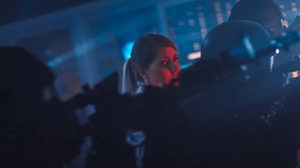 武装SWAT警察官のマスクチームは、デスクとコンピュータを備えた暗い押収されたオフィスビルで女性の人質を救助します。ライフルと懐中電灯を持つ兵士が前方に移動し、周囲をカバー. — ストック写真