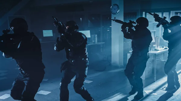 Masked Squad of Armed SWAT Police Officers Move in a Hall of a Dark Seized Office Building with Desks and Computers. Soldiers with Rifles and Flashlights Surveil and Cover Surroundings.