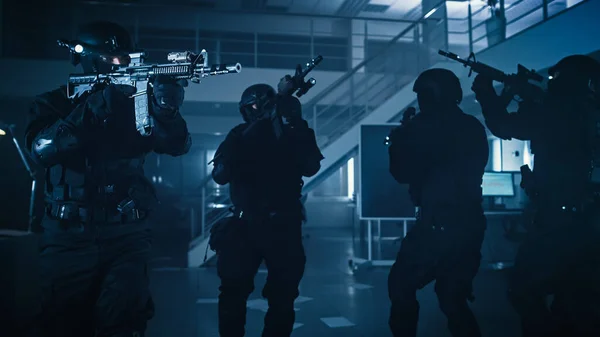 Maskierte bewaffnete SWAT-Polizisten stürmen ein dunkles Bürogebäude mit Schreibtischen und Computern. Soldaten mit Gewehren und Taschenlampen rücken vor und decken die Umgebung ab. — Stockfoto