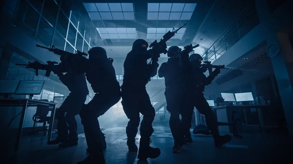 Gemaskerd team van gewapende SWAT politieagenten bewegen in een hal van een donker in beslag genomen kantoorgebouw met bureaus en computers. Soldaten met geweren en zaklampen Surveil en Cover Omgeving. — Stockfoto