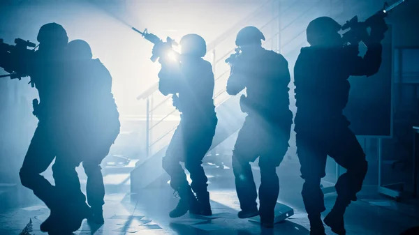 Masked Team of Armed SWAT Police Officers Move in a Hall of a Dark Seized Office Building with Desks and Computers. Soldiers with Rifles and Flashlights Surveil and Cover Surroundings.