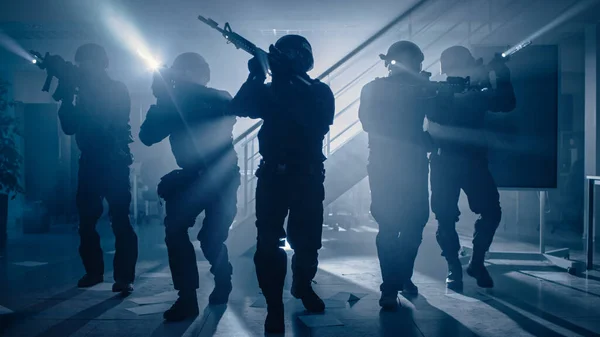 Equipe mascarada de policiais armados da SWAT se movem em um prédio de escritórios com mesas e computadores. Soldados com espingardas e lanternas Surveil e cobertura envolvente. — Fotografia de Stock