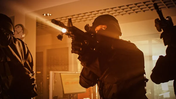 Masked Team of Armed SWAT Police Officers Move in a Hall of a Dark Seized Office Building with Desks and Computers. Soldiers with Rifles and Flashlights Surveil and Cover Surroundings.