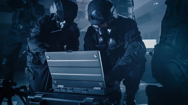 Equipe Mascarada de Policiais da SWAT armados com fuzis estão no prédio de escritórios Dark Seized com mesas e computadores. Soldado Abre um Computador Laptop para Planejar um Ataque Tático. — Fotografia de Stock