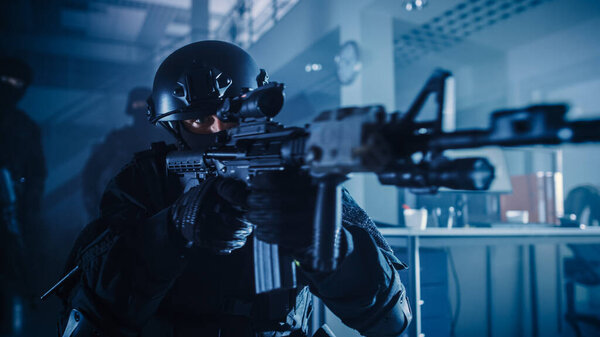 Close Up Portrait of Masked Squad Member of Armed SWAT Police Officers Who Storm a Dark Seized Office Building with Desks and Computers. Soldiers with Rifles and Flashlights.