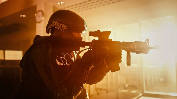 Närbild Porträtt av Masked Squad Medlem av väpnade SWAT poliser som stormar en mörk beslagtagen kontorsbyggnad med skrivbord och datorer. Soldater med gevär och ficklampor. Varma färger Sortering. — Stockfoto
