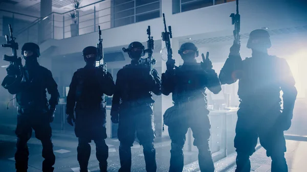 Masked Team of Armed SWAT Police Officers with Rifles are Posing After a Successful Office Building Siege. Soldiers Stand in a Row and Raise Firearms Up in the Air.