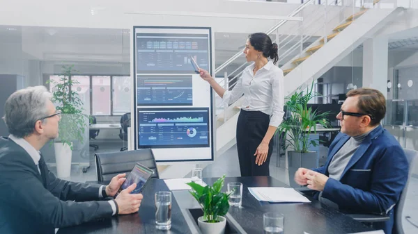 In the Corporate Meeting Room: Female Analyst Uses Digital Interactive Whiteboard for Presentation to a Board of Executives, Lawyers, Investors. Screen Shows Company Growth Data with Graphs