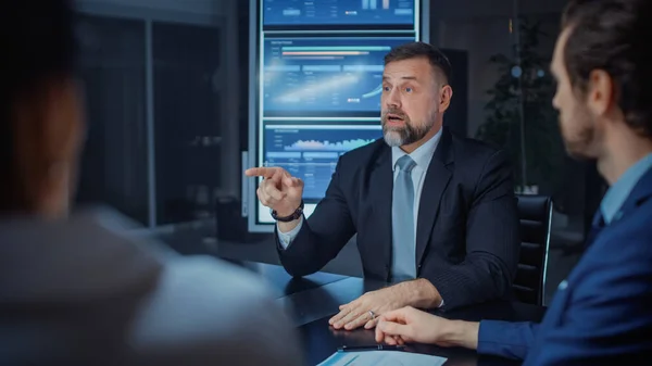 In the Modern Corporate Meeting Room: Diverse Group of Businesspeople, Executives and Directors Talking, Negotiating, Debating, Working with Documents, Planning Strategy. Late at Night in the Office