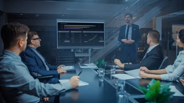 In the Corporate Meeting Room: Male Executive Talks and Uses Digital Interactive Whiteboard for Presentation to a Board of Directors, Investors. Screen Shows Growth Data. Late at Night Office
