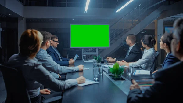Tarde da noite na sala de reuniões corporativas: Conselho de Administração, Executivos e Empresários Sentado na mesa de negociações, conversando e usando Green Mock-up Screen TV para videoconferência . — Fotografia de Stock