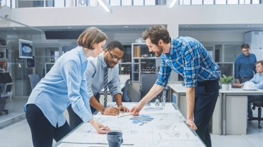 Endüstriyel Mühendislik Tesisi 'nde Endüstriyel Mühendis ve Usta Teknisyenle Çalışan Kadın Tasarımcı, Masa üzerinde yatan Motor Tasarımı ve Analizi Teknik Tasarımları var.