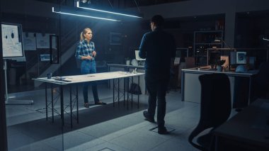 Karanlık Endüstriyel Tasarım Mühendislik Tesisi Erkek ve Kadın Mühendisler Konferans Masası Kullanarak Bir Planlar ve Teknik Çizimler Üzerinde Çalışıyor. Oda Bilgisayarlarında Ekranlar Motor Kavramını Gösterir