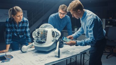 Robot Mühendislik Tesisi Üç Teknik Mühendisler Tekerlekli Robot Prototipi hakkında konuşuyor ve çalışıyor. Arkaplan Yüksek Teknoloji Araştırma Merkezi Ekranları Endüstriyel Tasarımı Gösteriyor.