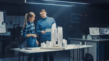Yaratıcı Mimarlık Bürosu 'nda İki Profesyonel Mühendis Şehir Bölgesi Modeli üzerinde çalışıyor. Şehir Planlamacıları İşlevsel İnşaat Modeli üzerinde çalışıyor. Konuşuyorlar ve Dijital Tablet Bilgisayarı kullanıyorlar