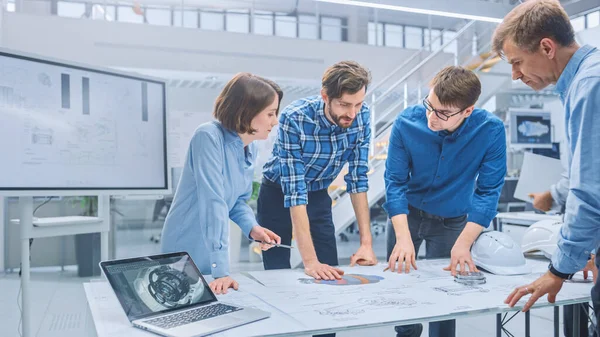 In the Industrial Engineering Facility: Diverse Group of Engineers and Technicians on a Meeting Gather Around Table with Engine Design Technical Drafts, Have Discussion, Analyse Technology — Stock Photo, Image