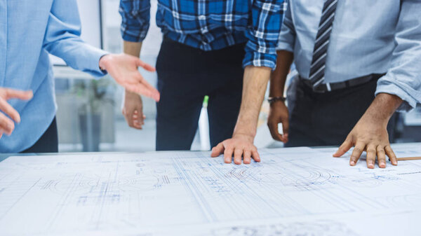 In the Industrial Engineering Facility: Diverse Group of Engineers and Technicians on a Meeting Gather Around Table Unravel Sheets of Engine Design Technical Drafts, Have Discussion, Analyse Drawings