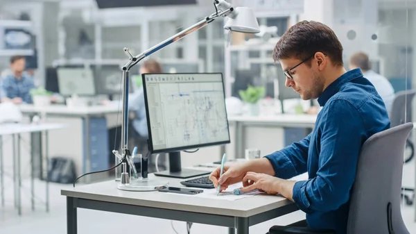 Sobre el hombro del ingeniero que trabaja con el software CAD en la computadora de escritorio, la pantalla muestra borradores técnicos y dibujos. En la planta de ingeniería de fondo especializada en diseño industrial —  Fotos de Stock