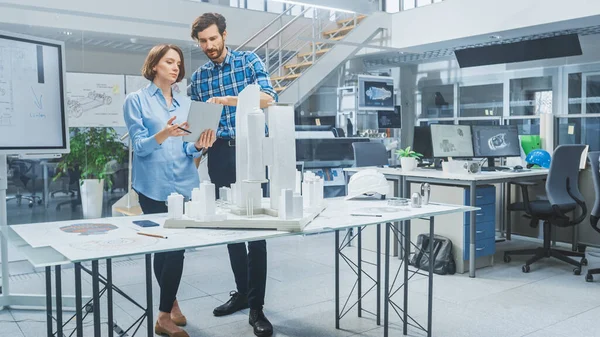 In Architectural Bureau: Architect and Engineer Talking, Using Digital Tablet Computer, Working on a Building Complex Prototype Project, Using City Model and Computers Running 3D CAD Software