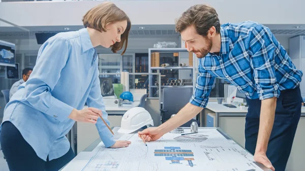 In the Industrial Engineering Facility: Young Female Designer Works with Chief Industrial Engineer, they have Discussion, Analyse and Correct Engine Design Technical Drafts that are Leying on the Table — Stock fotografie