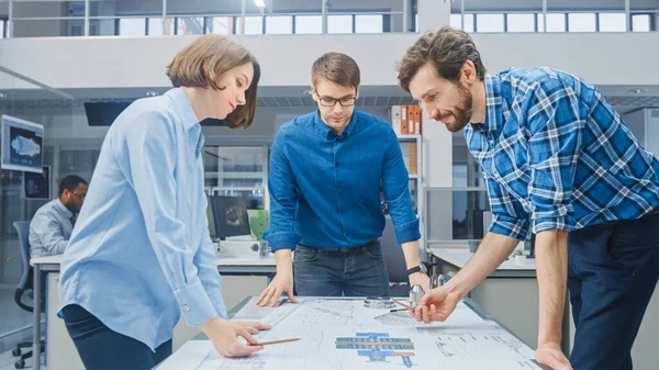 In the Industrial Engineering Facility: Female Designer Works with Industrial Engineer and Master Technician, They have Discussion, Analyse Engine Design Technical Drafts that Lying on the Table — 스톡 사진