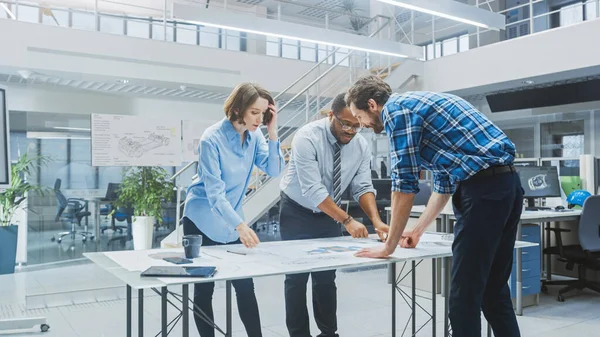 Na instalação de engenharia industrial: dois arquitetos e engenheiro-chefe, discutem e analisam esboços de protótipos de motores industriais usando mesa de conferência. — Fotografia de Stock