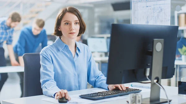 Na Instalação de Engenharia Industrial: Retrato da Engenheira Inteligente e Bela que Trabalha no Computador Desktop. No fundo Especialistas e técnicos que trabalham com rascunhos e desenhos — Fotografia de Stock