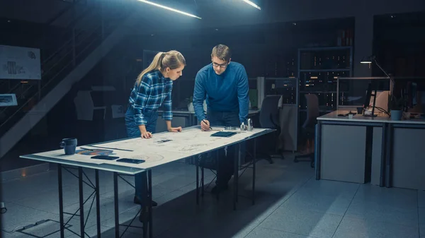 ダーク工業デザイン工学施設では、男性と女性のエンジニアは、会議テーブルを使用して青写真と技術図面に取り組んでいます。エンジンコンセプトを示すコンピュータが充実しています。 — ストック写真