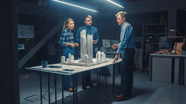In the Creative Architectural Bureau, Three Professional Engineers Work on a Model of a City District. Urban Planners Work on a Functional Building Model. People Working Late in the Evening