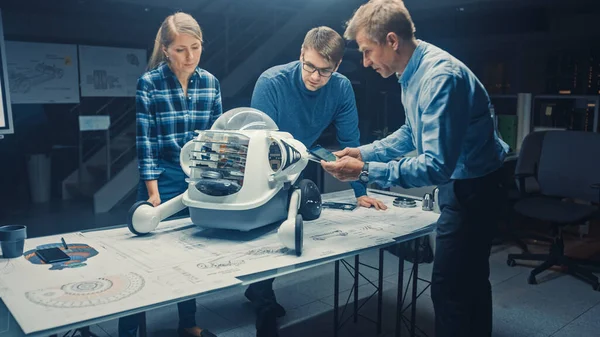 Zařízení pro robotické inženýrství Tři techničtí inženýři mluví a pracují na prototypu robota s koly. In the Background High Tech Research Center with Screens Show Industrial Design. Tmavá rána — Stock fotografie