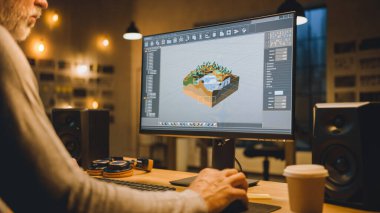 The Evening Creative Middle Aged Video Game Developer Works on a Desktop Computer with Screen 3D Videogame Level Design. Şık Yaratıcı Stüdyo Ofisi. Omzunun üstünden.