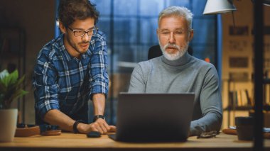 Yakışıklı Orta Çağ Girişimcisi ve Başarılı İşadamı Masasında oturan Laptop 'ta çalışıyor, Genç Meslektaşlarıyla Tartışıyor. Gülümsüyorlar ve eğleniyorlar. Akşamın geç saatlerinde şık bir ofis.